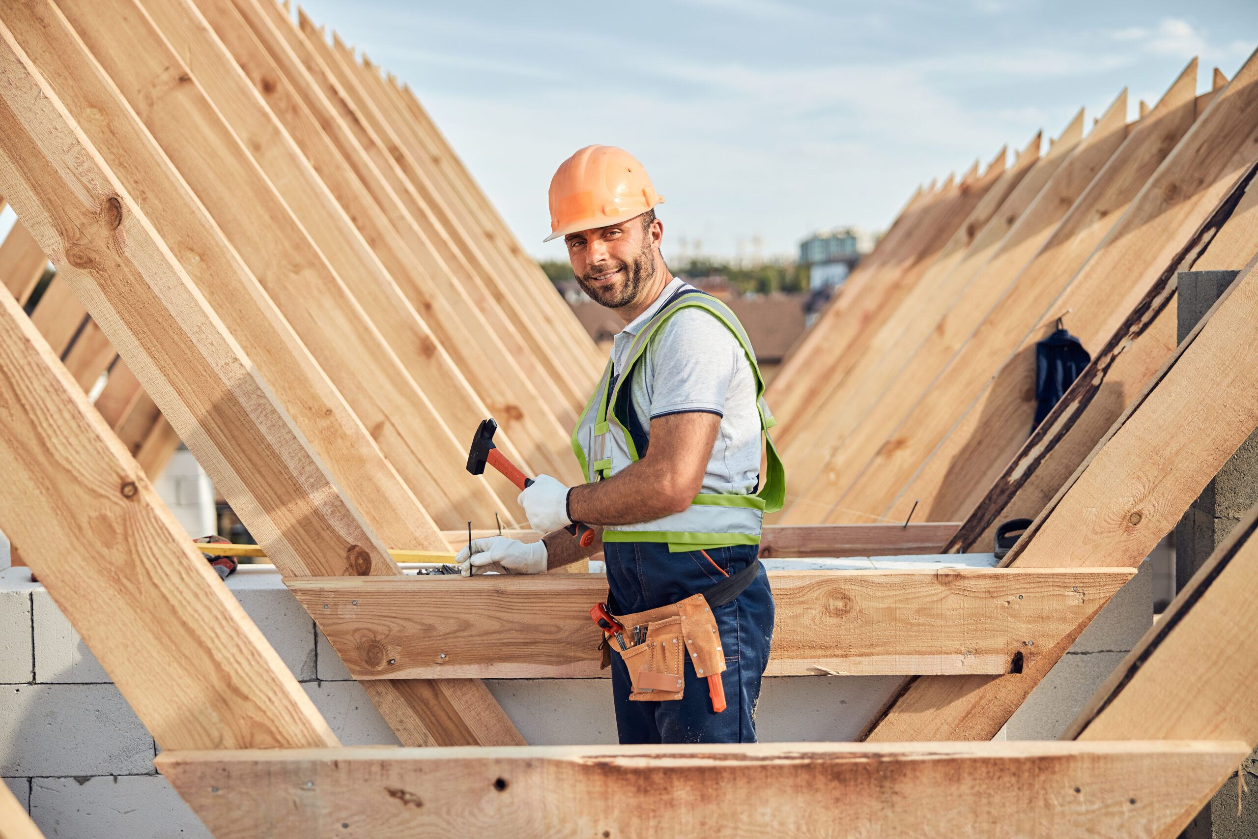 Brunette man wearing a hard hat and holding a hammer while looking at the camera