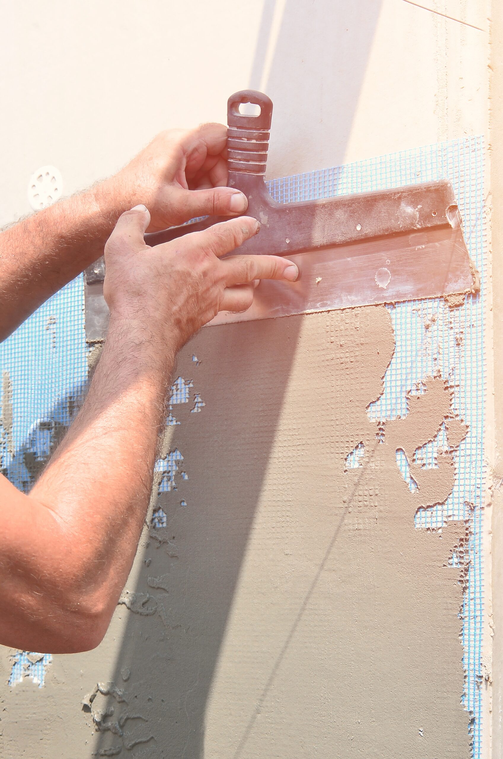 Hands of an old manual worker with wall plastering tools renovating house. Plasterer renovating outdoor walls and corners with spatula and plaster. Wall insulation. Construction finishing works