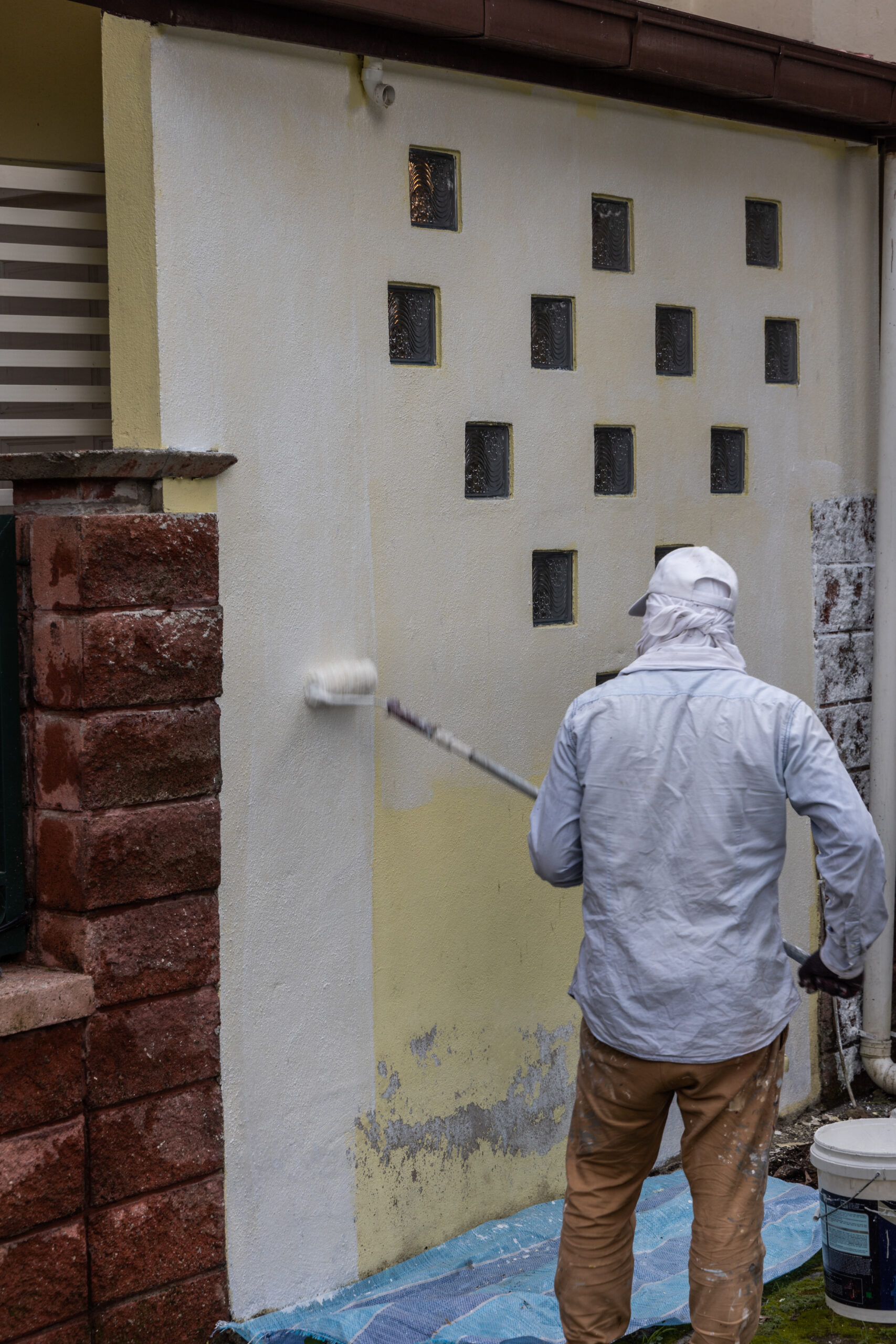 Painter worker adding undercoat foundation paint onto wall with roller as primer at residential building in renovation