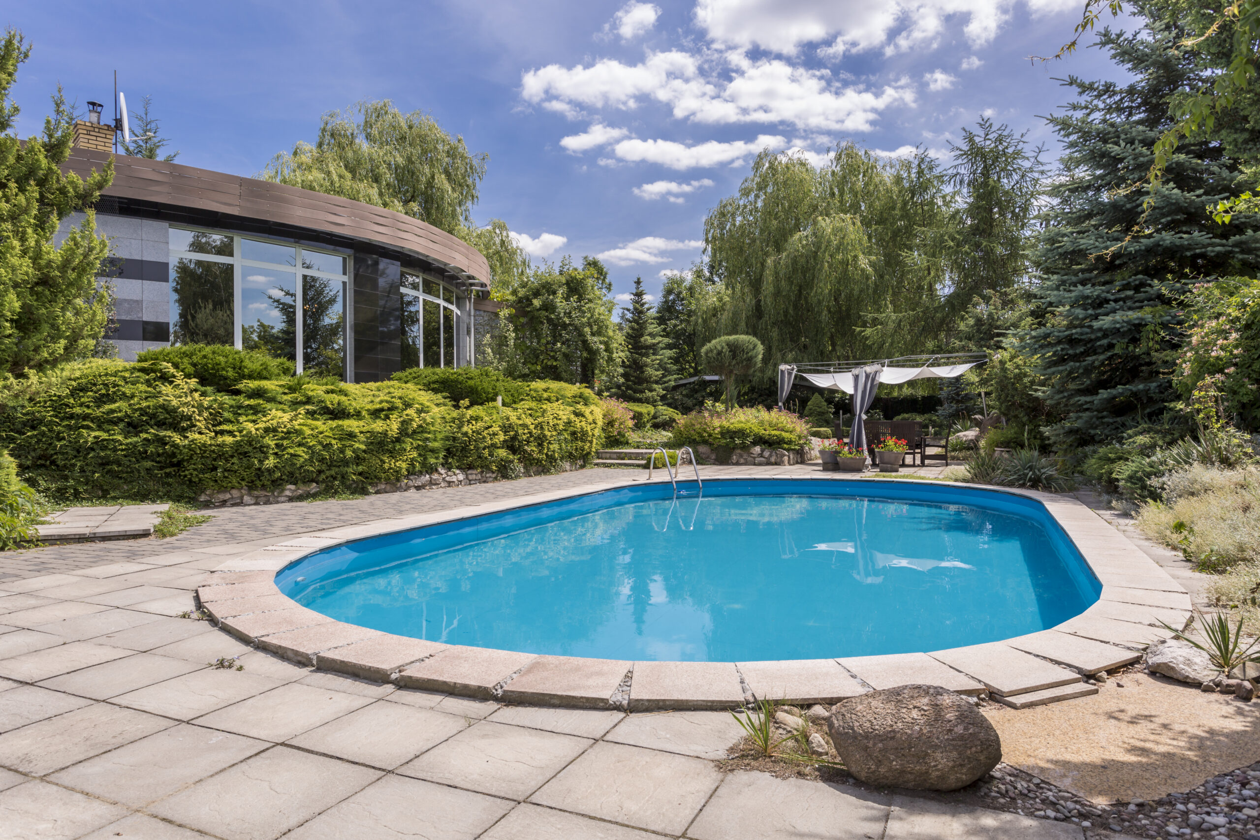 Oval swimming pool in big garden next to modern villa